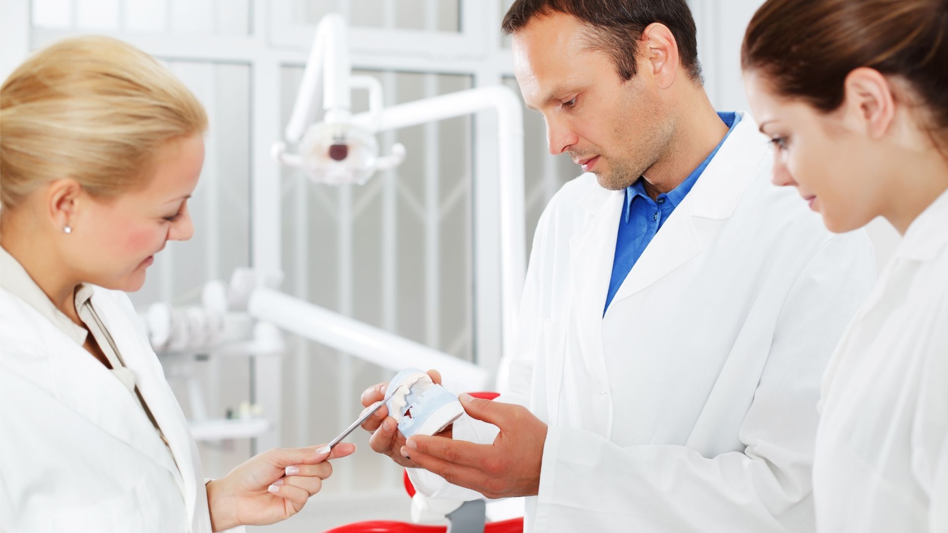 Ortodonta z modelem uzębienia w ręce dyskutuje z koleżankami nad leczeniem pacjenta.