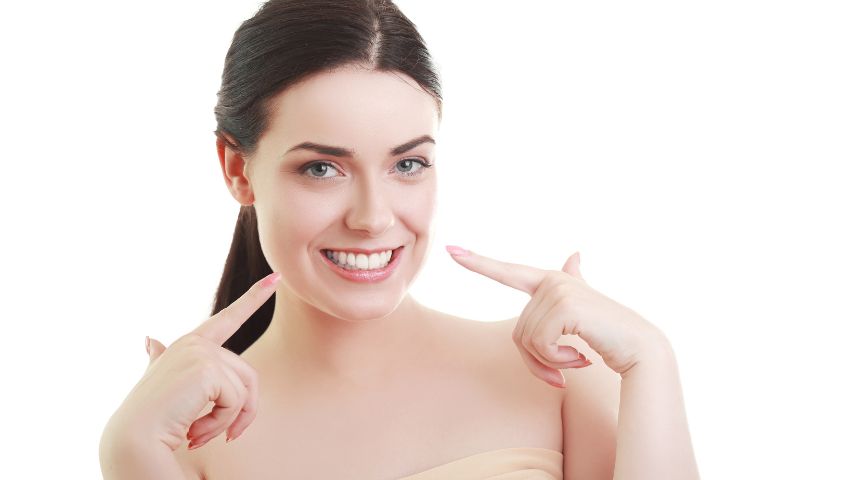 Uśmiechnięta kobieta wskazująca na swoje proste i białe zęby.